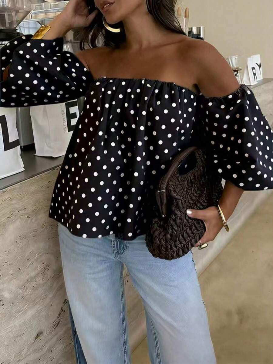 Woman wearing a black off-shoulder top with white polka dots and light blue jeans, holding a brown textured bag.