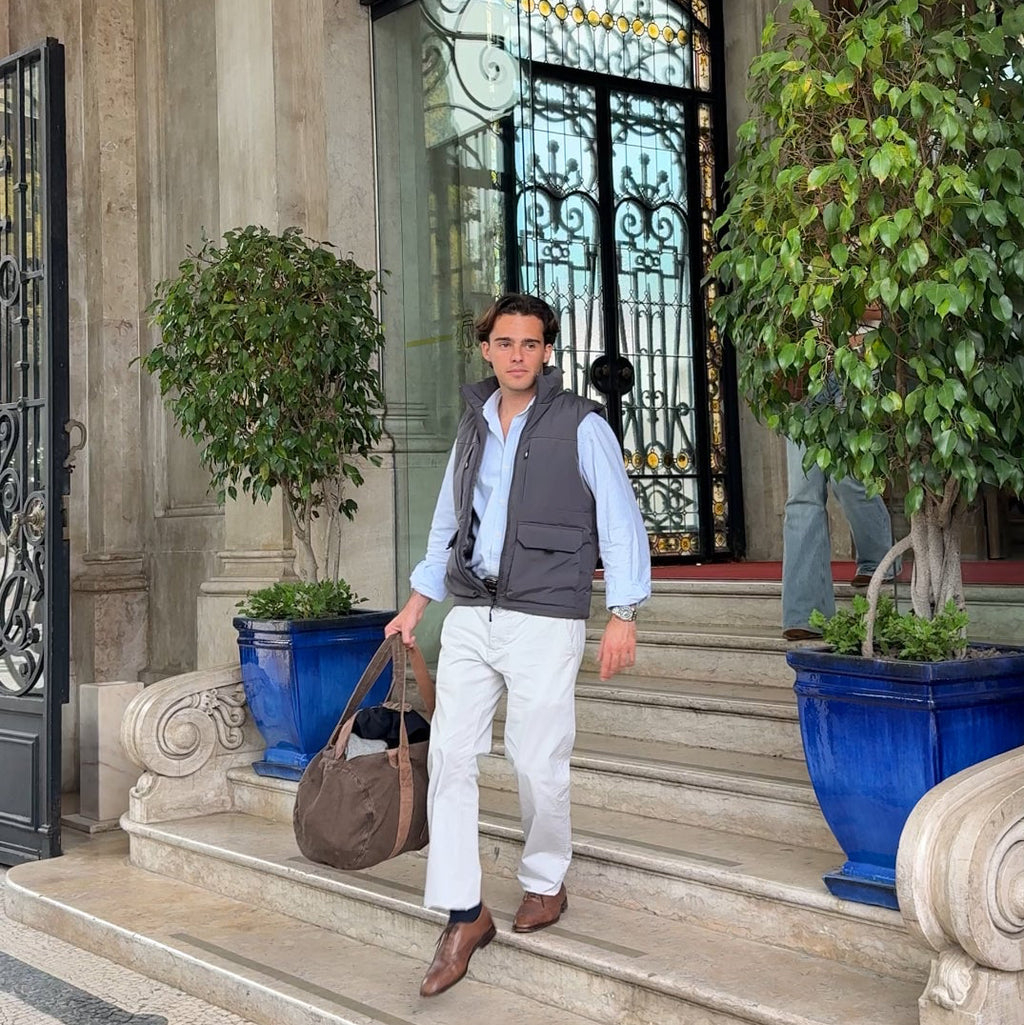 Man walking out of a building with decorative elements and plants. He brings a travel Mecenas duffel bag