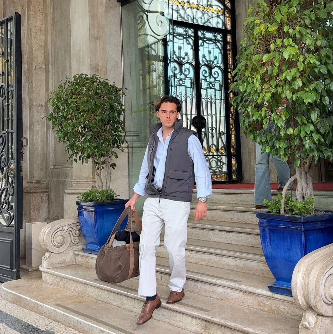 Man walking out of a building with decorative elements and plants. He brings a travel Mecenas duffel bag
