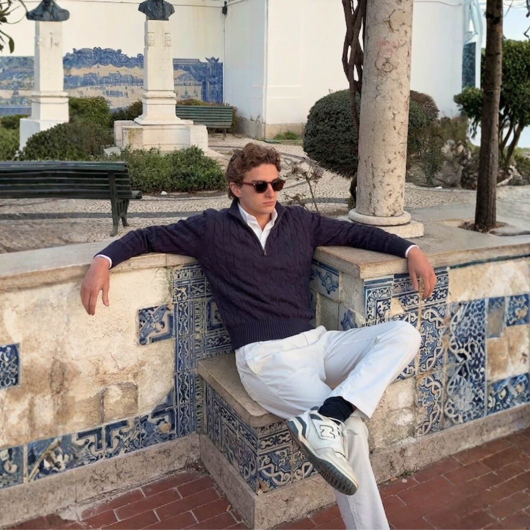 Man sitting on a decorative wall with a building and garden in the background