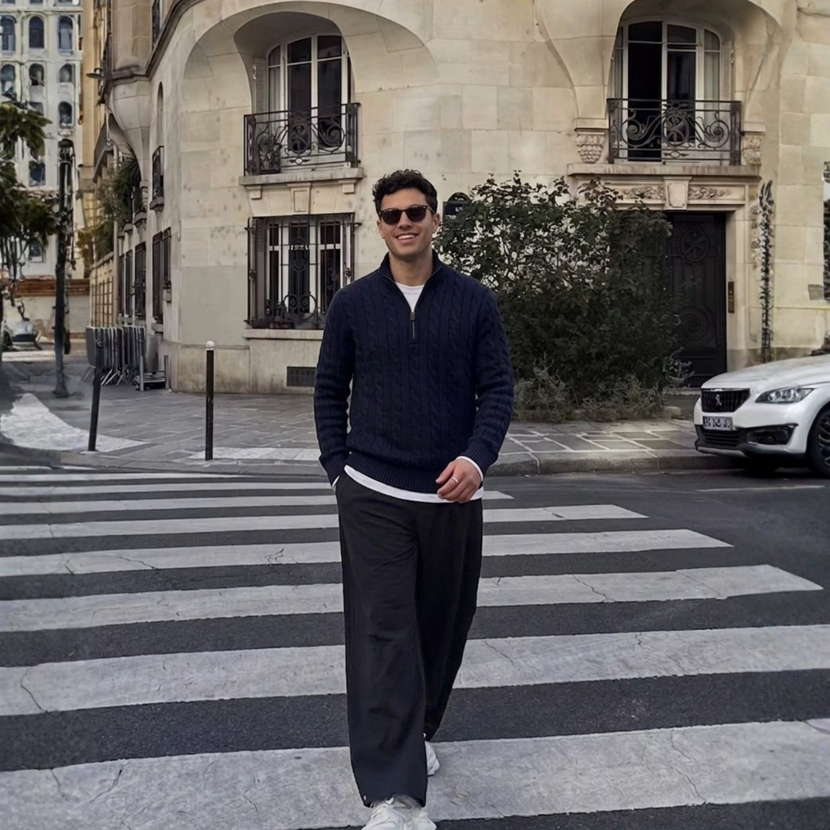 Man walking on a zebra crossing in an urban setting with buildings and cars in the background.