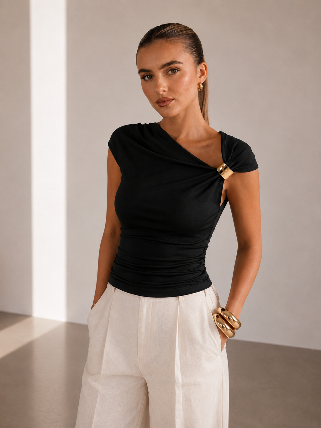 Woman wearing a black top with a unique design and white pants against a neutral background
